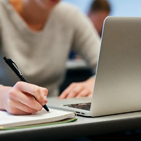 Person writing in notepad beside a laptop